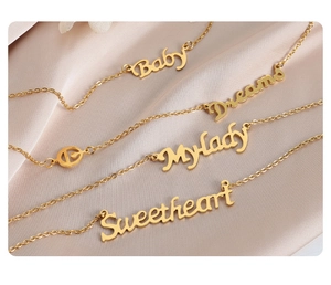 Dettaglio di quattro collane d'oro con pendenti Baby e Dreams su seta color champagne