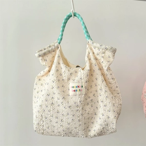 Detail of floral bubble crepe tote with green woven handle and rainbow embroidered label