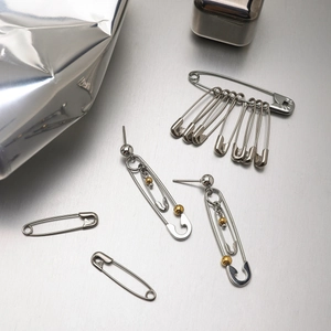 Detail view of silver paperclip earrings with gold beads on industrial metal surface