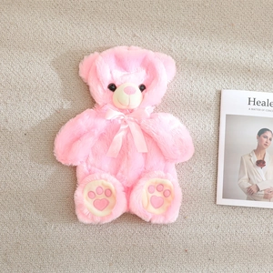 Pink plush teddy bear with neck bow and heart paw prints on a cozy home background