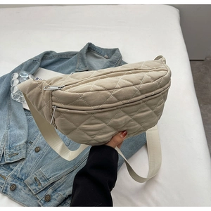 Detail of beige quilted crossbody bag with adjustable strap on denim jacket background