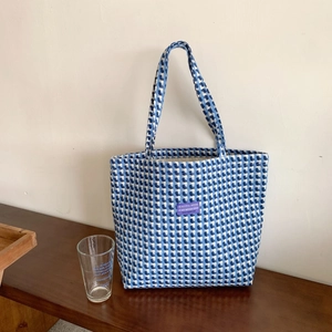 Detailed texture of blue and white checkered woven tote bag with purple label on wood table