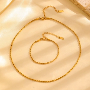Detailed view of a gold-plated twisted rope chain necklace and bracelet set on beige silk
