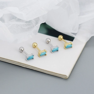 Detailed view of silver and gold turquoise rectangular stud earrings on a white surface
