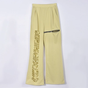Detail of light yellow wide-leg pants with distressed cut-outs and silver zipper pockets