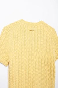 Dettaglio del top in maglia gialla con trama a treccia e scollo rotondo rifinito bene