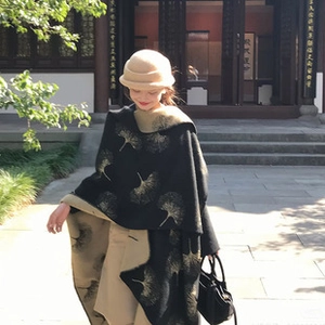 Detail of a thick black pashmina shawl with gold ginkgo leaf pattern and beige felt hat
