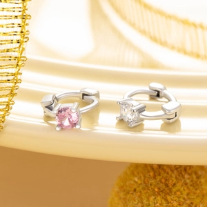 Elegante silberne Creolen mit rosa und klaren Zirkonia vor edlem goldfarbenem Hintergrund