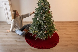 Close-up of red cable knit Christmas tree skirt on wooden floor by fireplace