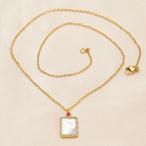 Detail of gold necklace with rectangular shell pendant and red gemstone on fabric