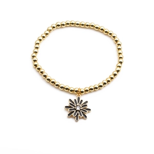 Gros plan sur un bracelet à billes dorées avec pendentif marguerite en émail noir et zircon