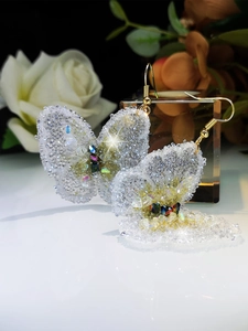 Macro shot of butterfly crystal drop earrings with sparkling resin grains and gold hooks