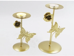Detail of two gold metal candle holders featuring 3D rose and butterfly accents on white background