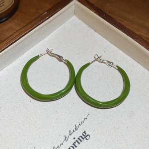 Detail view of grass green enamel C-shaped hoop earrings on a light fabric tray