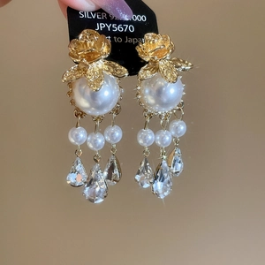 Close-up of golden rose earrings with large pearls and 925 silver fringe crystals