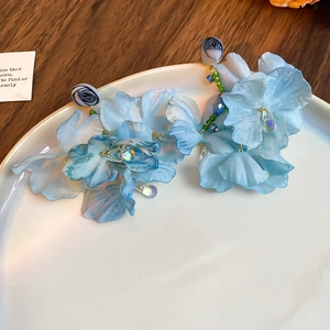 Blue fabric flower earrings with green beads and drop charms on a white plate