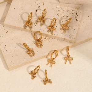 Luxuriöse goldene Edelstahl-Schleifenohrringe mit Zirkonia auf einem steinernen Hintergrund