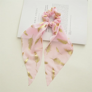 Macro shot of pink chiffon scrunchie with gold feather print and elegant long ribbon