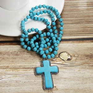 Detail of bohemian turquoise beaded necklace with a large silver cross pendant on wood