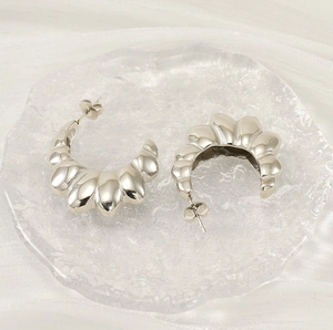 Macro shot of silver C-shaped scalloped earrings on textured glass with soft fabric