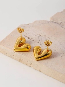 Macro detail of glossy gold irregular heart stud earrings on beige stone base