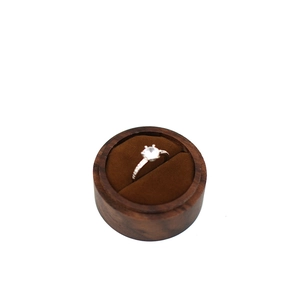 Detail view of a silver diamond ring presented inside a round brown wooden jewelry box