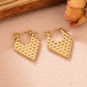 Détail de boucles d'oreilles en U dorées avec motif géométrique texturé en pyramide