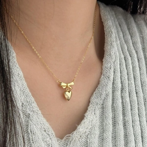 Elegant gold bow heart necklace for women worn on a grey textured knit sweater