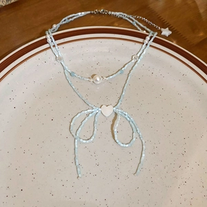 Detail of light blue beaded necklace with pearl heart and star charms on a ceramic plate