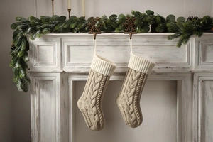 Detail of knit Christmas stockings with cable pattern hanging on a white fireplace