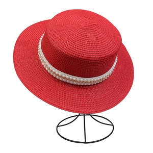 Close-up of red woven straw boater hat featuring pearl beads and gold chain decoration