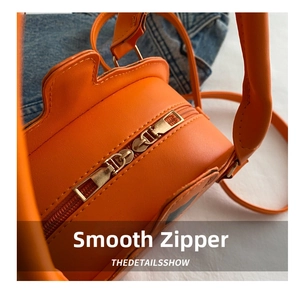 Detailed close-up of smooth metal double zippers on bright orange fruit shaped crossbody bag