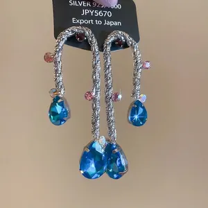 Dettaglio macro di orecchini d'argento con cristalli a goccia blu e accenti rosa