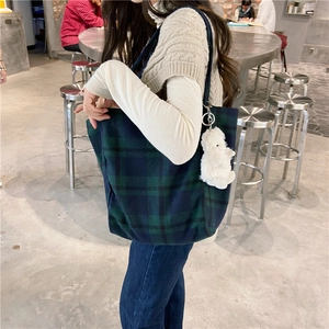 Close-up of green plaid wool tote bag with a white plush lamb keychain charm in a cafe