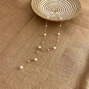 Detailed view of elegant gold Y-shape pearl necklace on rustic jute and ceramic background