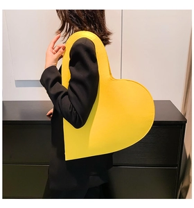 Close-up of oversized yellow heart-shaped leather bag styled with a black blazer