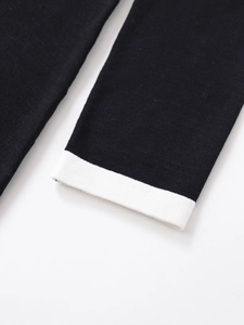 Close-up of a minimalist black knit dress showing contrasting white cuff detail and texture