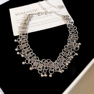 Detailed macro view of silver metallic bohemian necklace with round bell charms on black velvet