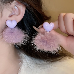 Detail of purple heart stud earrings with soft plush pom poms on a model ear