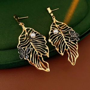 Detailed macro view of golden hollow leaf earrings with white pearl and butterfly accents