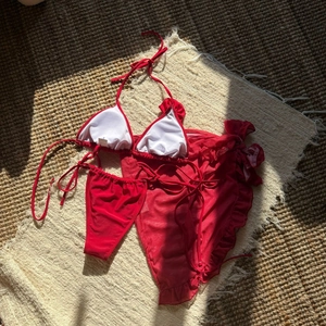 Detailed view of red three-piece bikini set with ruffle mesh skirt on a beach mat