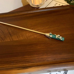 Close-up of a gold metal hair stick with green jade-like cylinder and floral details