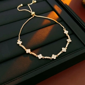 Close-up of golden adjustable bracelet with zircon clover motifs on a black tray
