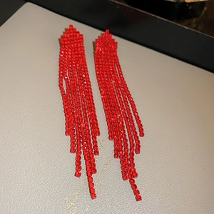 Detailed view of red rhinestone tassel earrings with silver needle on a texture card
