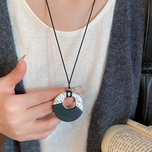 Detail of a minimalist geometric round pendant on a black cord shown on a model