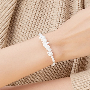 Detailansicht eines weißen Natursteinarmbands an einem Model mit beigem Strickpullover