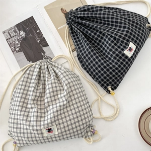 Detail of plaid canvas drawstring backpacks with cartoon cat labels on white table