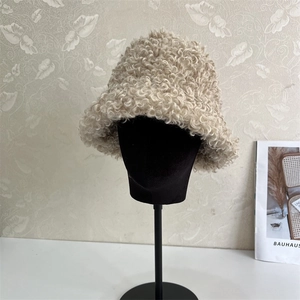 Close-up of off-white plush bucket hat with lamb wool texture on a display stand