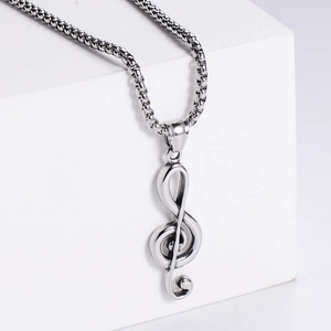 Detailed view of silver treble clef music pendant on a sturdy box chain over white blocks