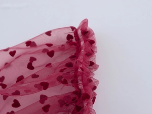 Détail du tissu en maille rouge avec motifs de cœurs en velours et bords plissés
